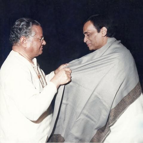 Shri Purshottam Das Jalota draping a shawl on Kavi Narayan Agrawal
